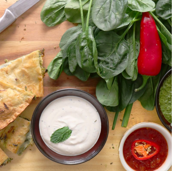 Several different types of yogurt dips and chutneys laid next to flatbread slices.