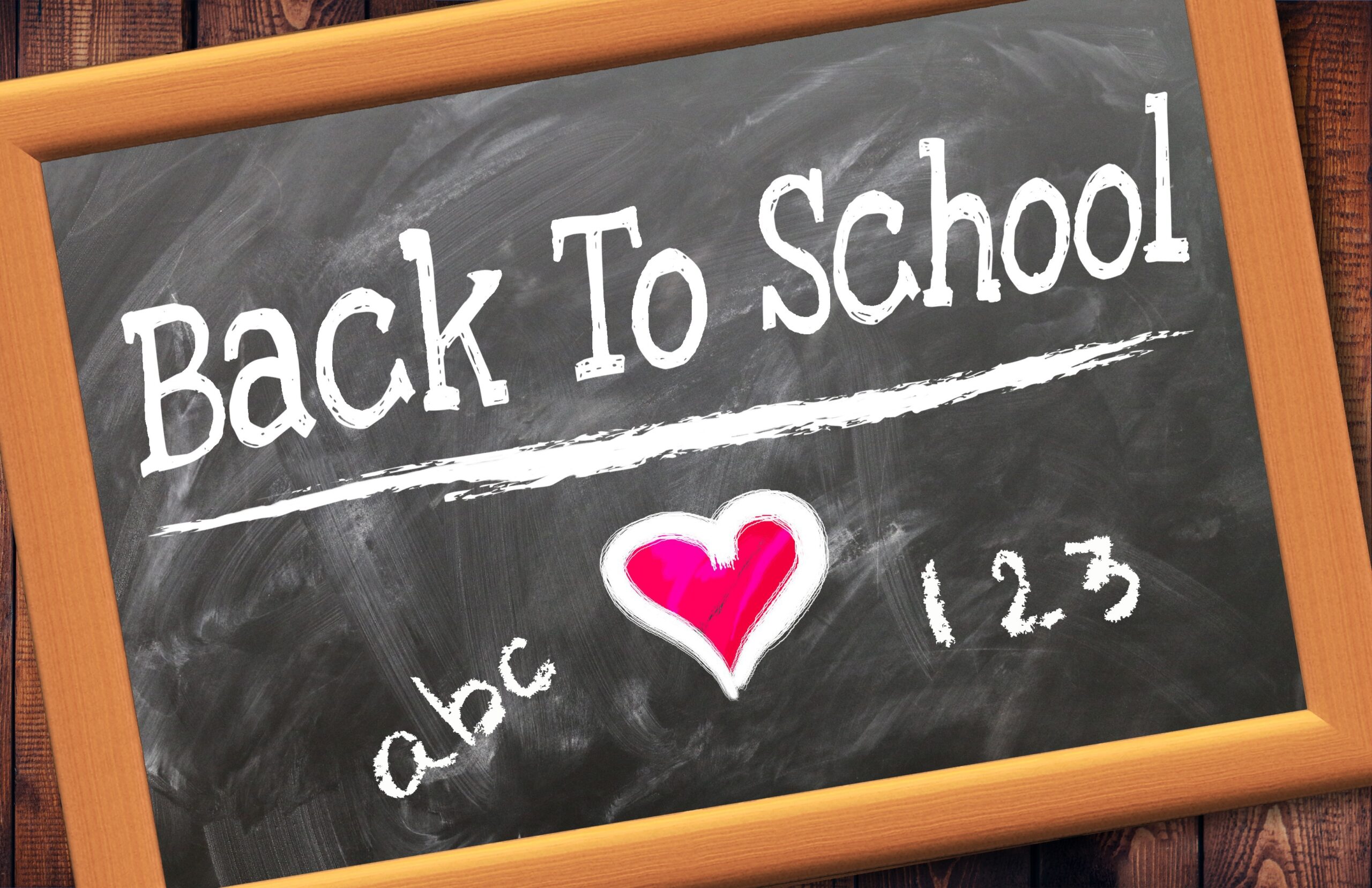 "back to school" is written on a black chalkboard in white chalk. There is also "abc", "123", and a read heart on the chalkboard.